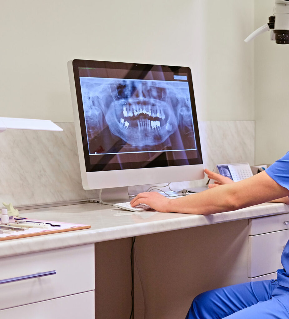 Male dentist looking at teeth x-ray on the computer in a dentist office.