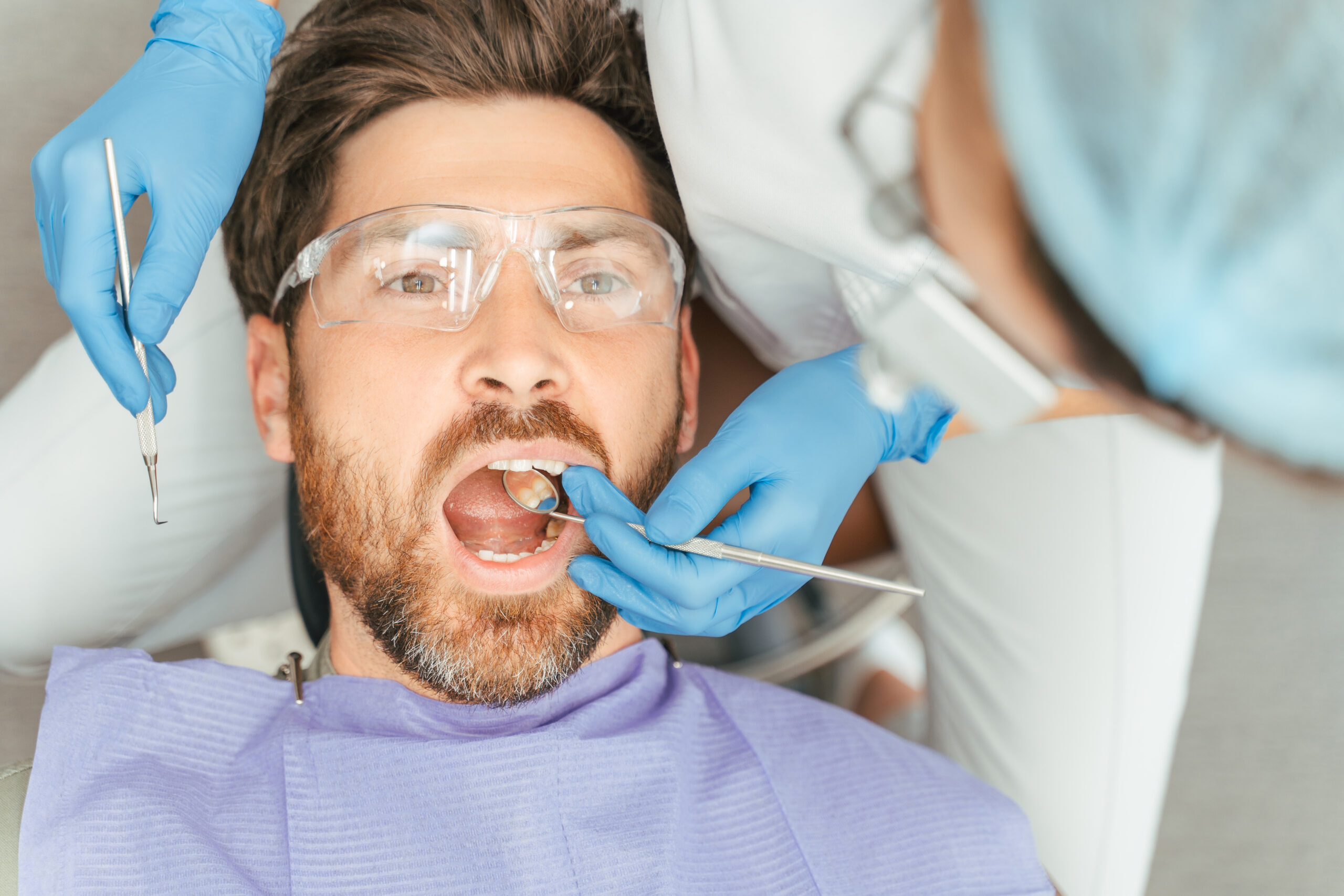 Bearded male patient in dental chair wearing protective glasses during treatment