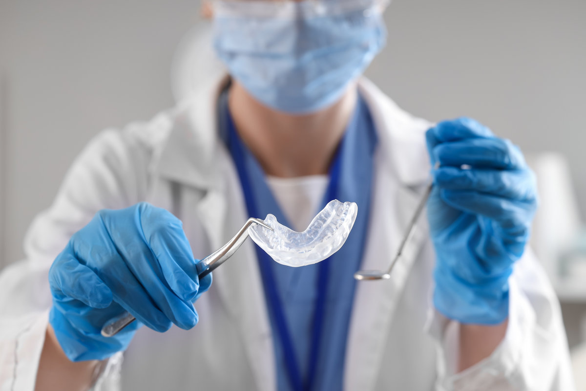 Female dentist with occlusal splint and tools on grey background, closeup