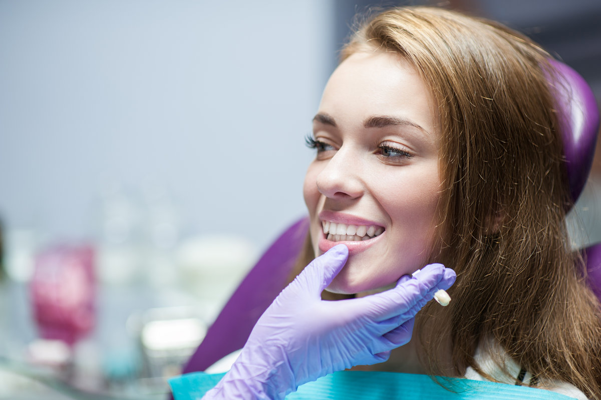 Young woman smiling in dental chair while dentist holds a crown near her mouth