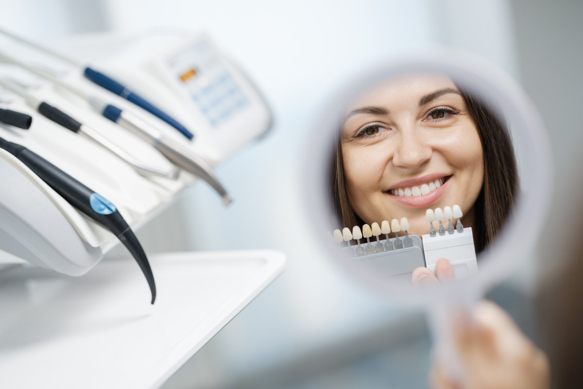 Cheerful young girl is visiting dental clinic and looking at reflection of her smile in the mirror after treatment