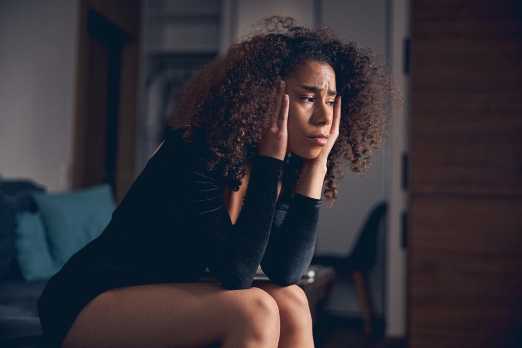 Sad young African American lady in a stylish evening dress sitting alone on the sofa